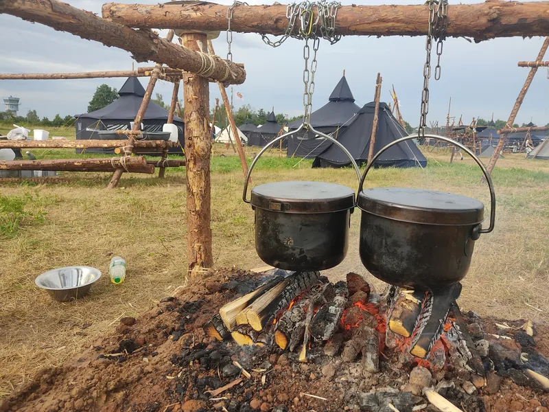Zwei große Kochtöpfe hängen über einem Lagerfeuer