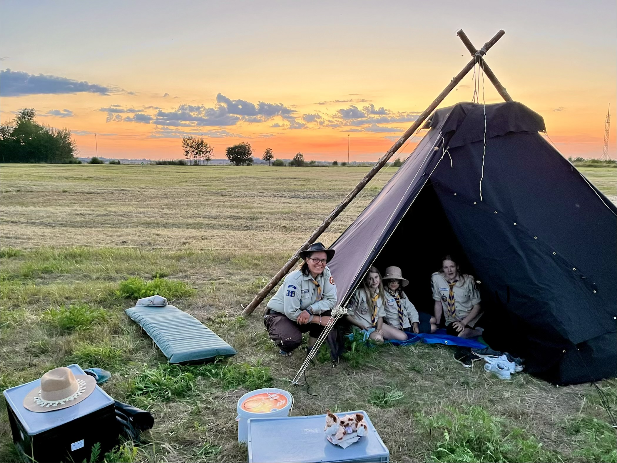 Eine Leiterin und drei M&auml;dchen in Kluft sitzen bei Sonnenuntergang vor einer Kohte