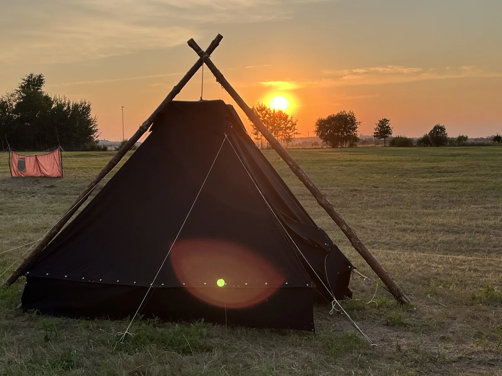 Eine Kohte im Abendlicht, daneben geht die Sonne unter