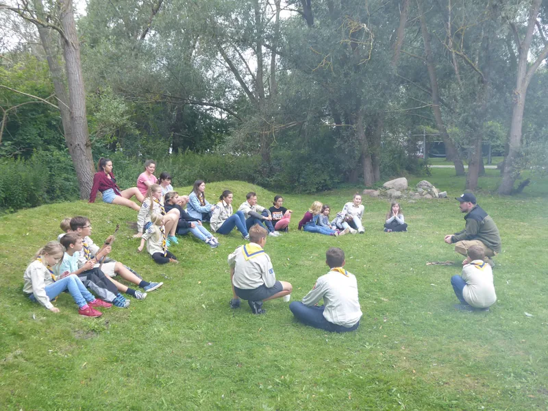 Kinder und Leiter sitzen im Kreis auf der Wiese am Weidendom im IGA Park