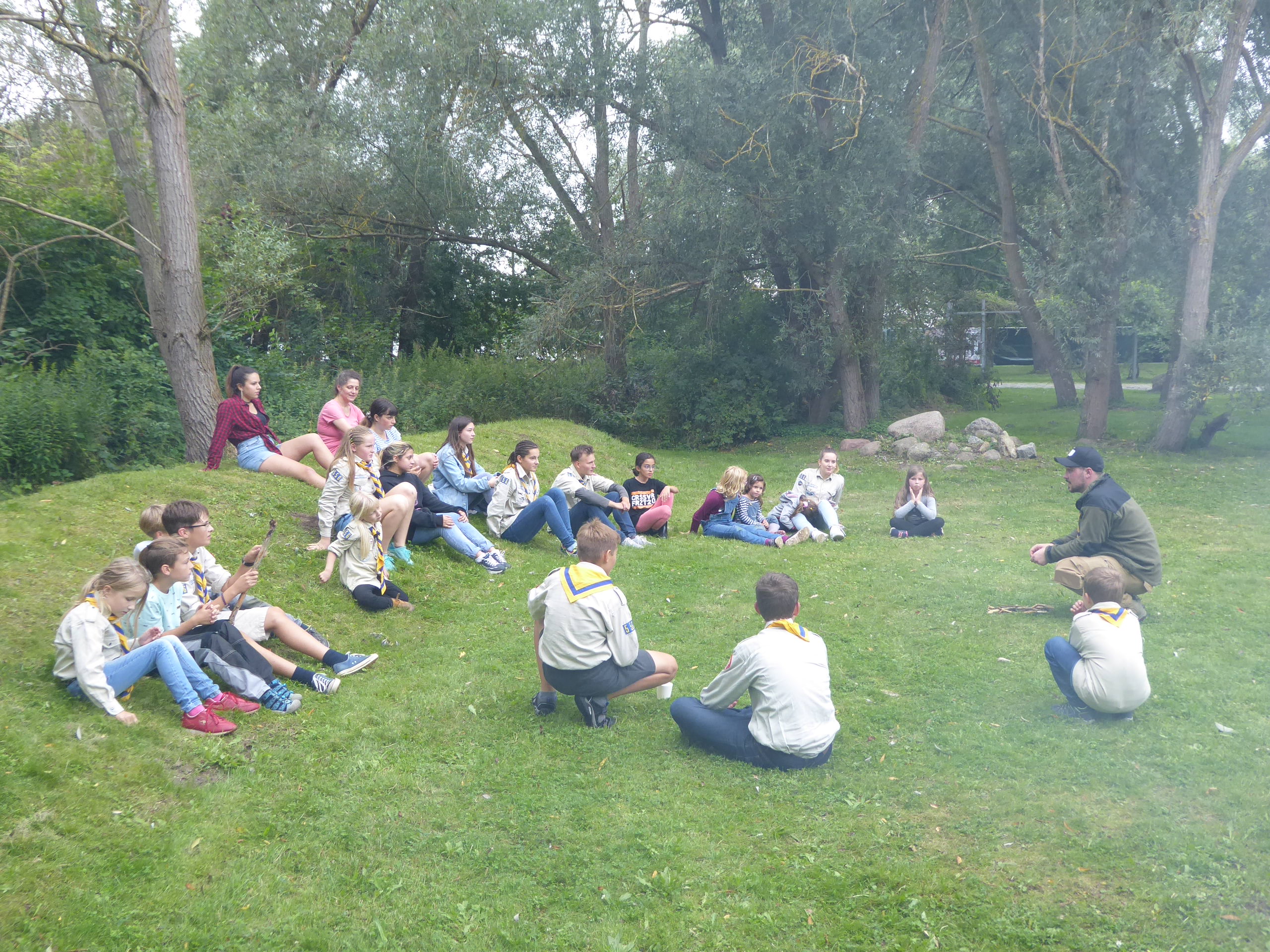 Kinder und Leiter sitzen im Kreis auf einer Wiese im IGA Park
